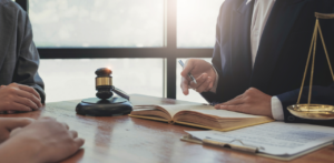 A lawyer pointing at a document while consulting with clients at a desk, with a gavel and scales of justice nearby