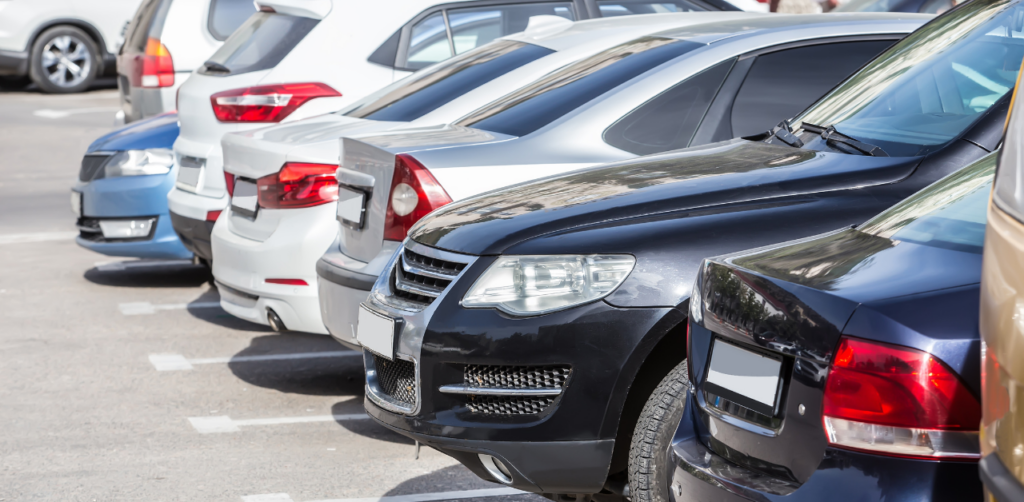 Row of parked cars in a parking lot, showing the rear ends of various vehicles in different colors under daylight