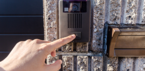 Hand pressing the button on a video doorbell mounted on a brick wall