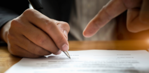 Hands signing legal document as another points, illustrating estate planning help