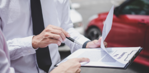 Two people discussing and pointing at an insurance policy document on a clipboard, with cars visible in the background