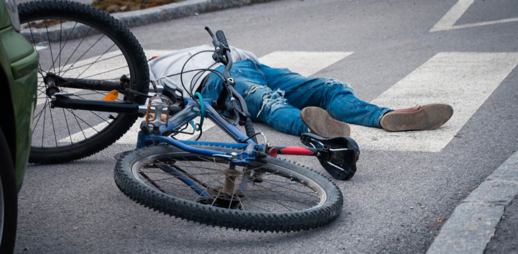Person lying on the ground near a fallen blue bicycle at a pedestrian crossing, suggesting a road accident