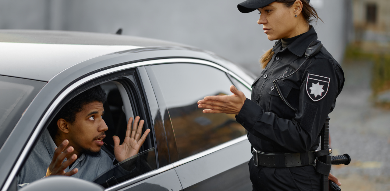 Female police officer talking to a driver seated in a car, with the driver gesturing with open hands