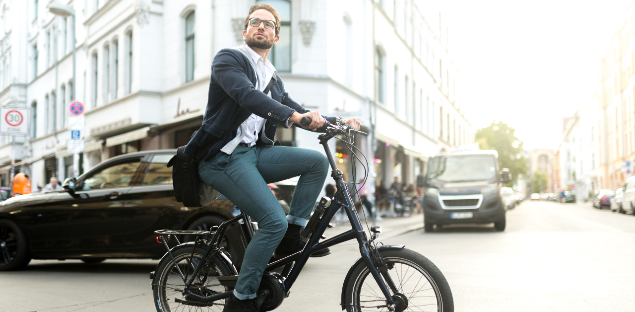 Well-dressed man riding a bicycle on a city street surrounded by cars, vans, and urban buildings