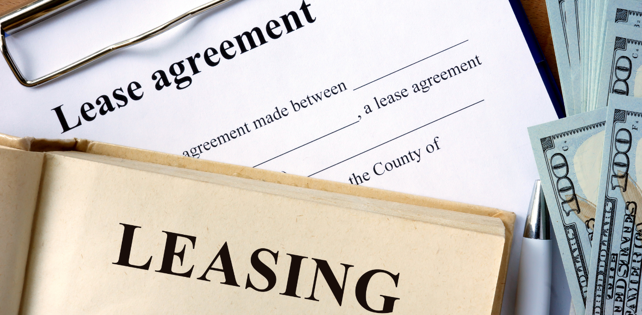 Lease agreement with pen, cash, and leasing book shown on a clipboard