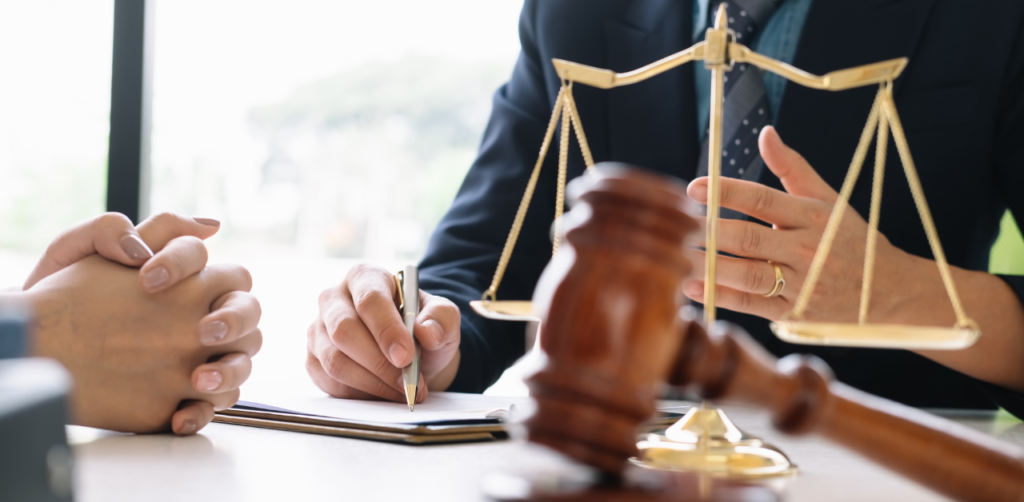 Two people in formal attire discussing paperwork at a desk with a gavel and scales of justice in the foreground