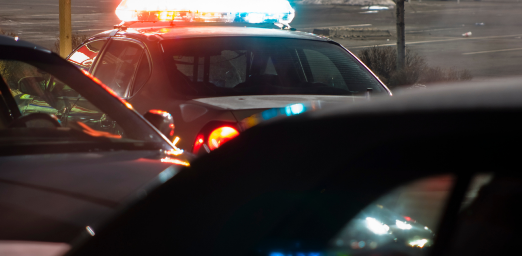 Police car with flashing red and blue lights at night, partially visible through the window of another vehicle