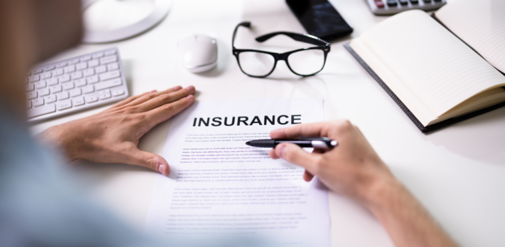 Person reviews an insurance document at a desk with a pen, keyboard, glasses, and notebook nearby