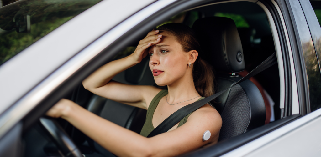 A worried woman sitting in a car, resting her hand on her forehead while wearing a seatbelt