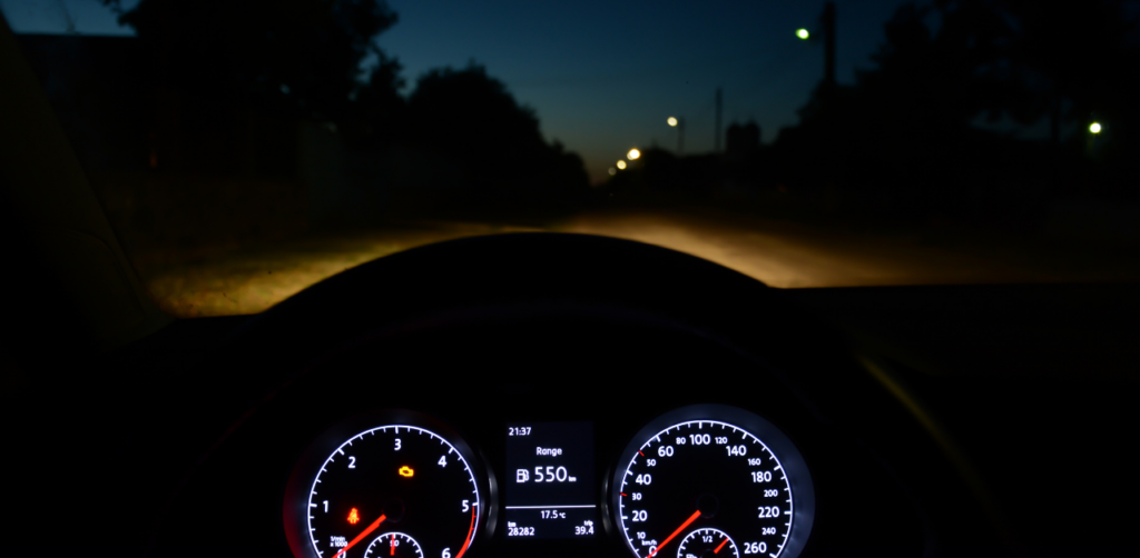 Nighttime view from a car dashboard showing illuminated gauges and a dark road ahead