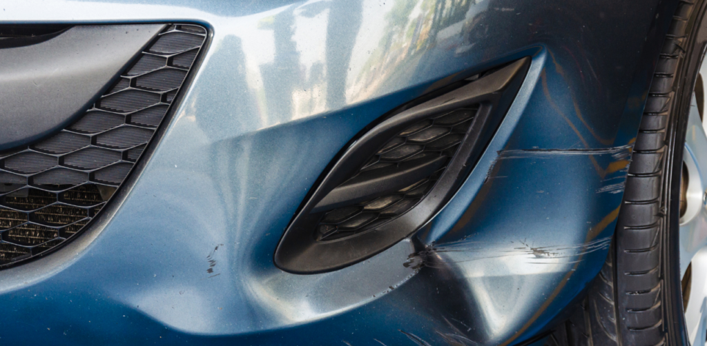 Close-up of a dented car bumper with scratches and impact marks near the front tire