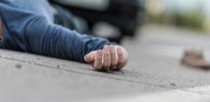 Injured person lies motionless on the road near a vehicle, hand extended on the pavement