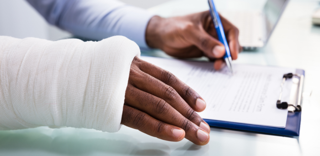 Person with arm in a cast signs a medical or insurance form on a clipboard at a desk