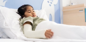 Young girl with a cast on her arm resting in a hospital bed after a car accident injury