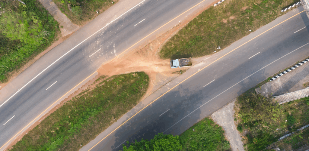 Aerial view of a rural road where a truck takes an informal dirt path between divided highways, highlighting dangerous U-turn behavior