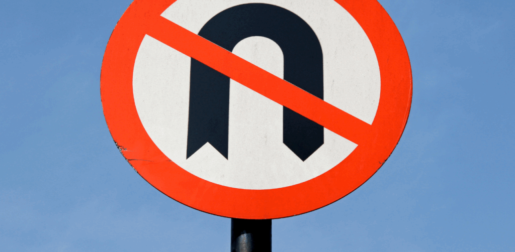 Close-up of a no U-turn traffic sign with a red circle and slash over a curved black arrow, warning drivers against illegal turns
