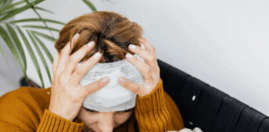 A woman with a head bandage sits holding her head in pain, indicating a recent injury or concussion