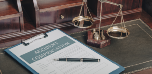 A legal document titled Accident Compensation next to a pen and golden scales of justice on a lawyer's desk