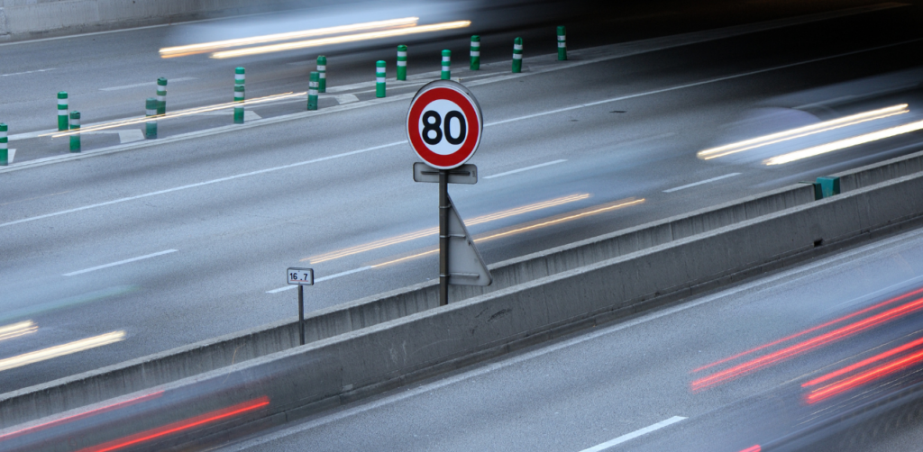 Speed limit sign on a highway with blurred streaks of headlights and taillights from fast-moving cars