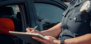 Close-up of a police officer writing a report on a notepad beside a parked car