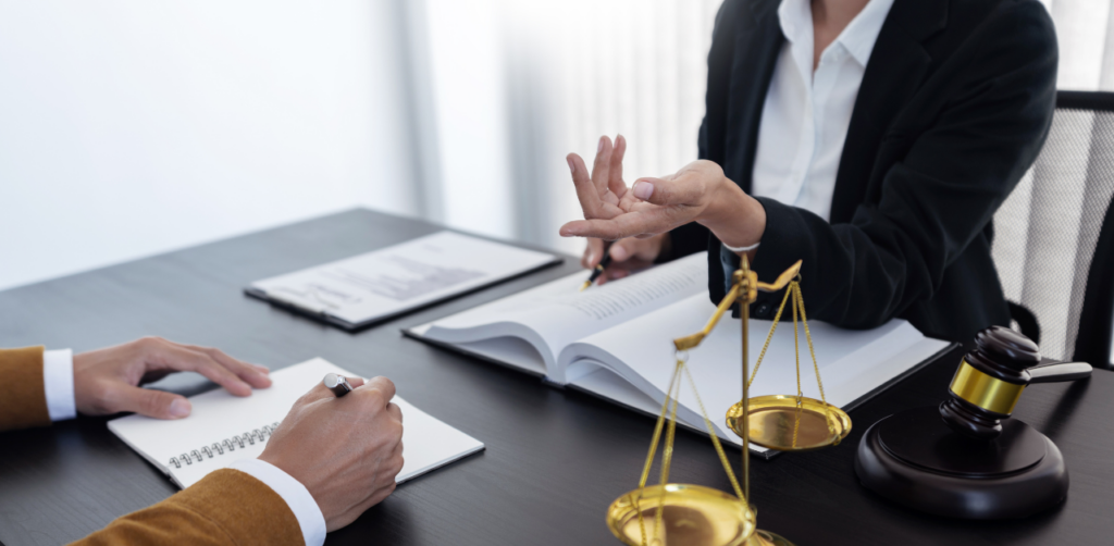 Lawyer discussing a case with a client across a desk with open books, legal scales, and a gavel
