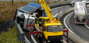 Yellow tow truck lifting an overturned semi-truck on a curved highway