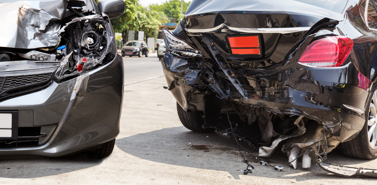 Two cars with significant rear-end damage, showing crumpled and broken bumpers, parked on a city street