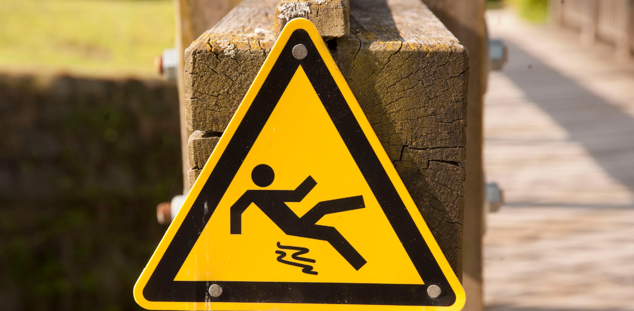 Yellow caution sign showing a figure slipping, mounted on a wooden post