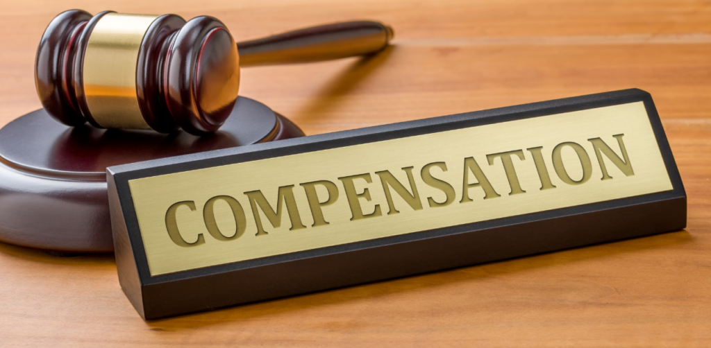 A gavel rests next to a sign labeled Compensation, on a wooden surface