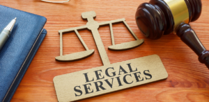 A wooden scale of justice and a gavel sit on a desk next to a notebook, with a sign that reads Legal Services