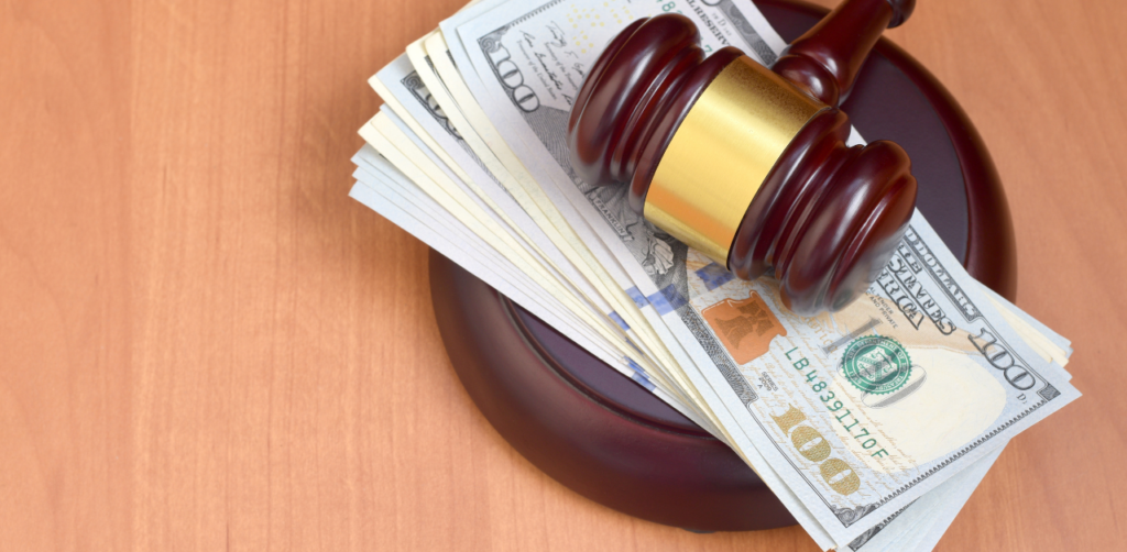 Wooden gavel resting on a stack of hundred-dollar bills on a wooden surface