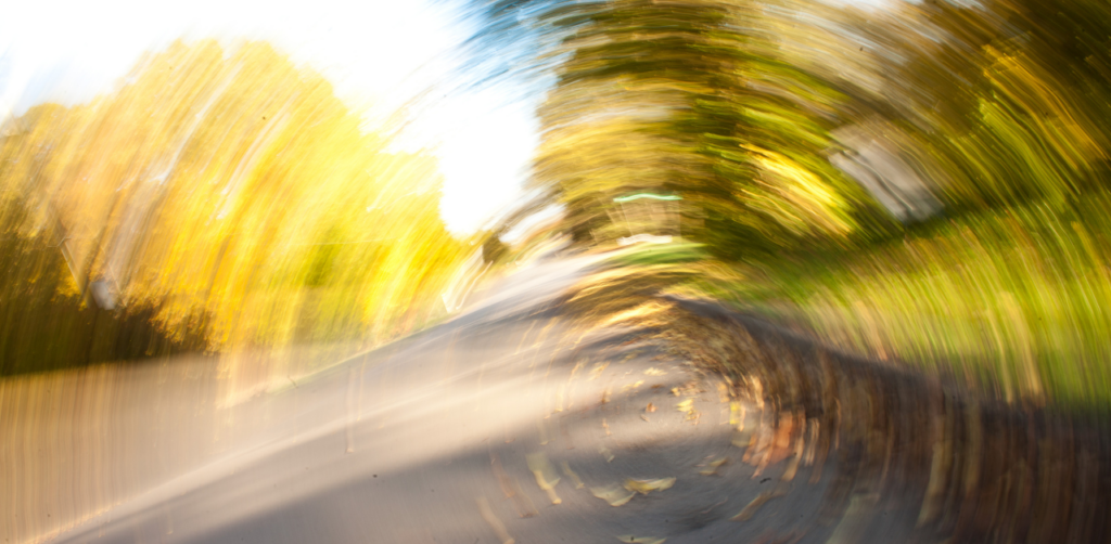 A blurred, spinning view of a road lined with trees, creating a dizzying or disoriented effect, possibly simulating a loss of control