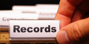 A close-up of a hand pulling out a file tab labeled Records from a set of organized folders