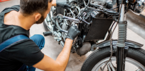 A mechanic working on a motorcycle engine, wearing gloves and using tools to adjust parts