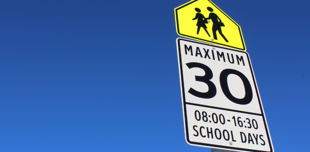 A school zone speed limit sign showing Maximum 30 during school hours, set against a clear blue sky