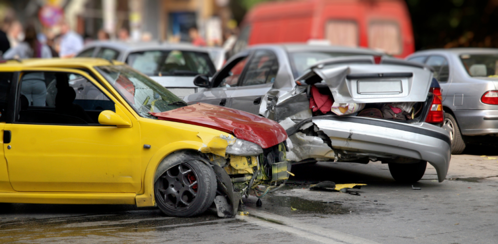 A yellow car with front-end damage and a silver car with rear-end damage after a collision on a busy street