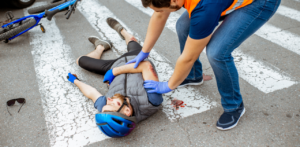 Person in a high-visibility vest assisting an injured cyclist lying on a crosswalk, with a bike and sunglasses nearby