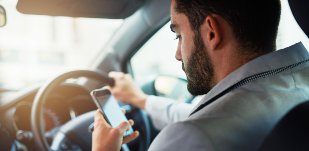 Man in a car looking at his phone while driving, with one hand on the steering wheel