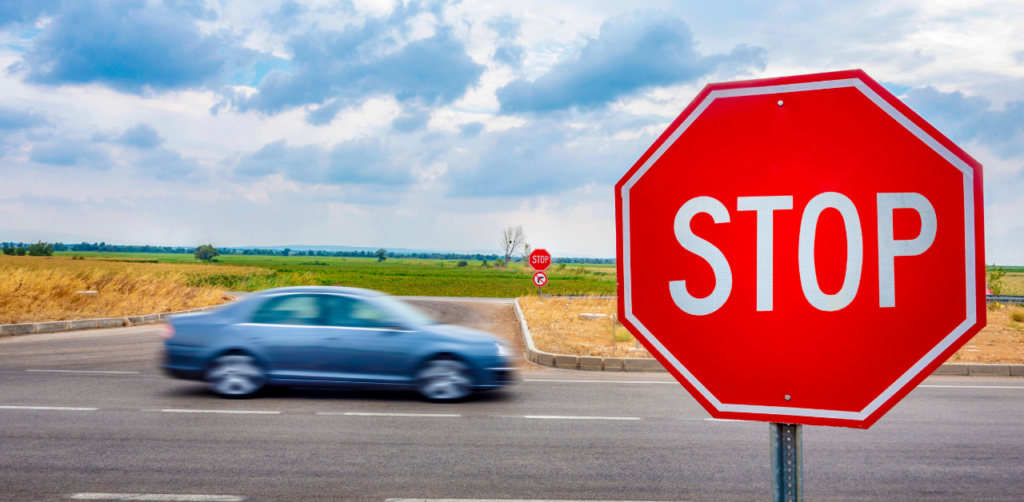 Red stop sign in focus, with a speeding car driving through an intersection in the background