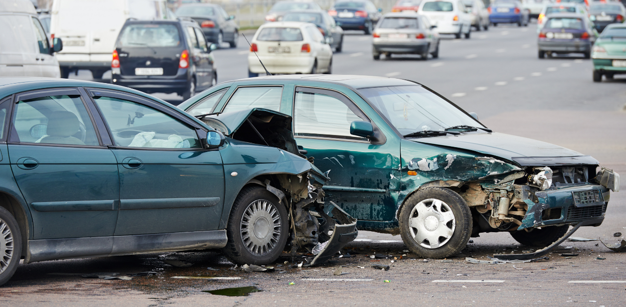 Two damaged cars at an intersection, showing severe front-end and side damage with traffic in the background