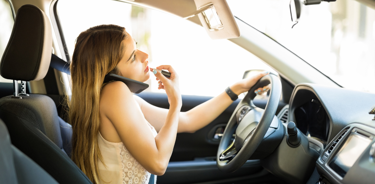 Woman multitasking while driving, holding a phone between her shoulder and head while applying lipstick