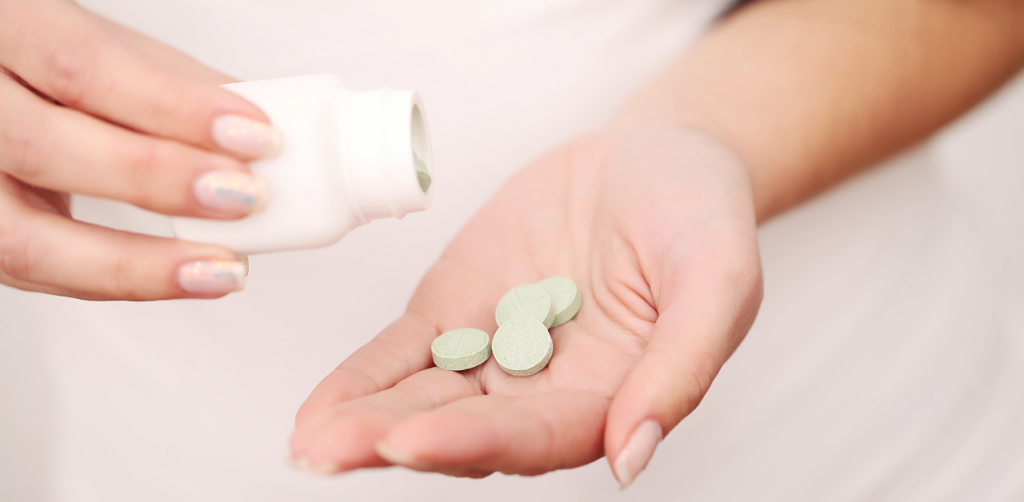 Close-up of a hand pouring green tablets from a white bottle into the palm, against a white background