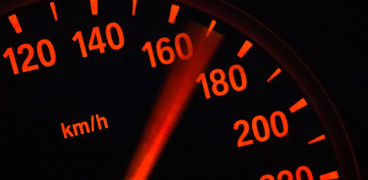 Close-up of a speedometer with the needle pointing past 160 kmh, glowing red in the dark