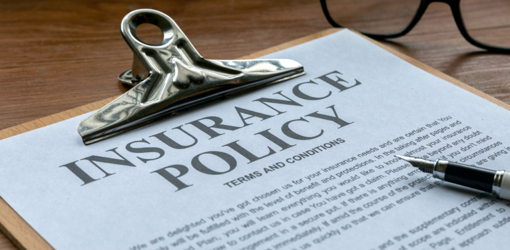 Close-up of an insurance policy document clipped to a board, with a pen and glasses in the background