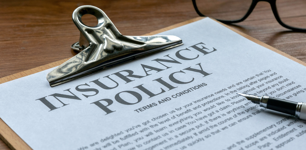 Close-up of an insurance policy document clipped to a board, with a pen and glasses in the background