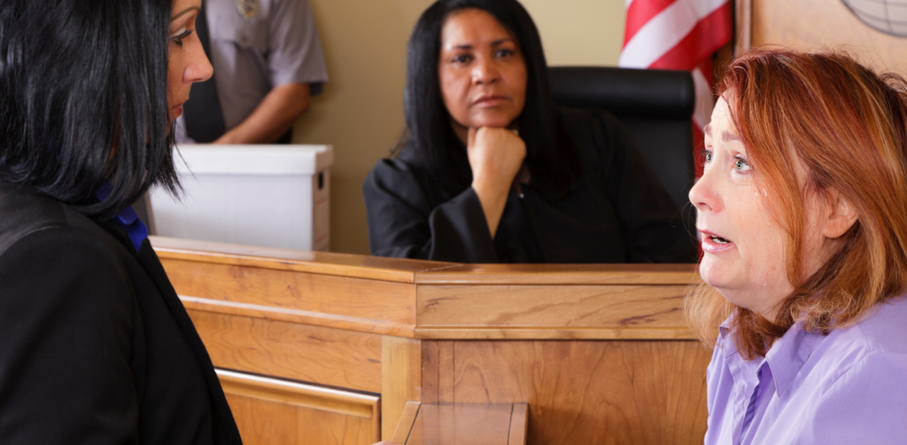Distressed woman testifies in court, crying while speaking to a lawyer, with a judge observing from the bench in the background