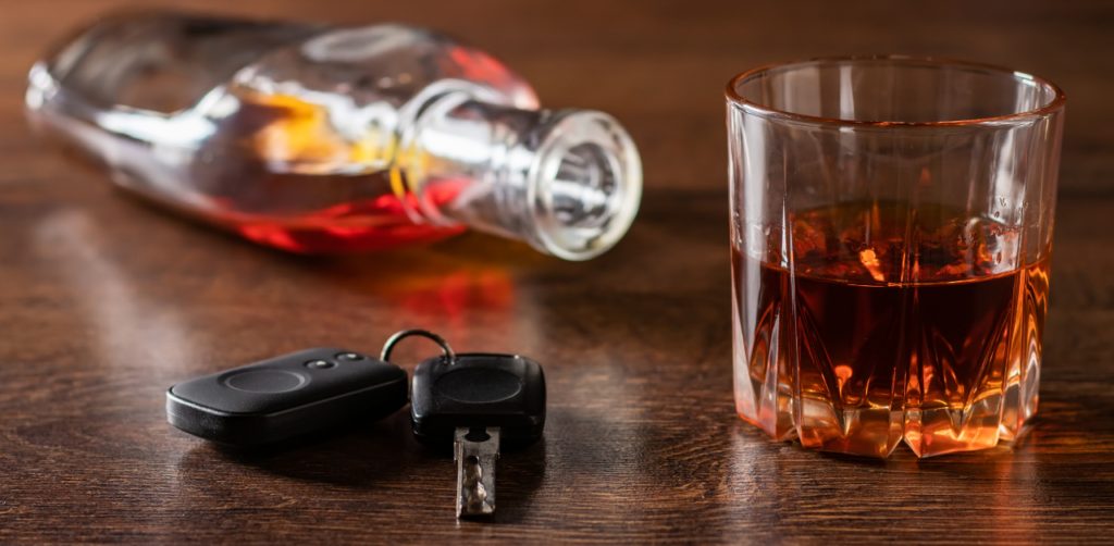 Glass of whiskey, a car key, and a bottle of alcohol on a wooden table, symbolizing the dangers of drinking and driving