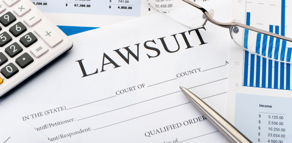 Lawsuit document with a pen, calculator, financial charts, and eyeglasses placed around it