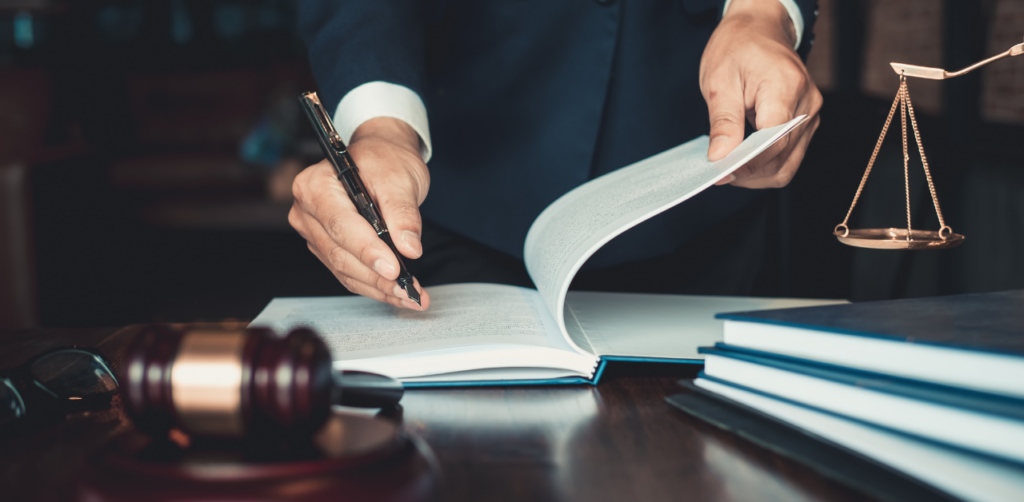 Lawyer or professional reviewing and signing documents at a desk, with a gavel and scales of justice nearby