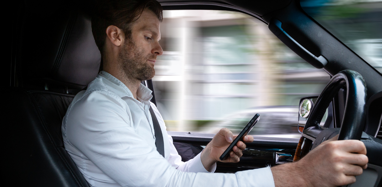 Man driving a car while looking at his phone, depicting distracted driving
